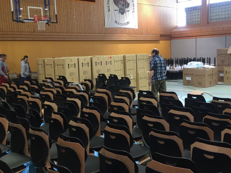 Aula mit Stuhlreihen und angelieferten Kartons